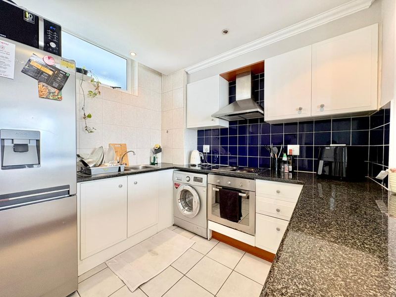 A functional kitchen featuring granite countertops, dark blue tiled backsplash, built-in oven, hob, extractor fan, and white cabinetry with tiled flooring.