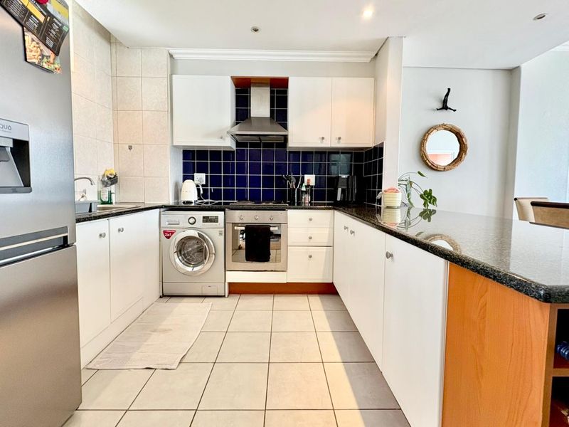 Modern kitchen featuring white cabinetry, granite countertops, a tiled backsplash, built-in oven with extractor fan, and an integrated breakfast bar.