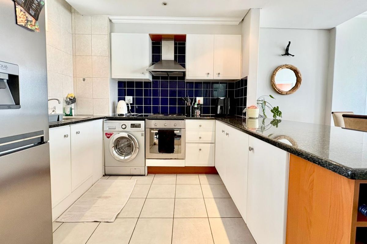 Modern kitchen featuring white cabinetry, granite countertops, a tiled backsplash, built-in oven with extractor fan, and an integrated breakfast bar.
