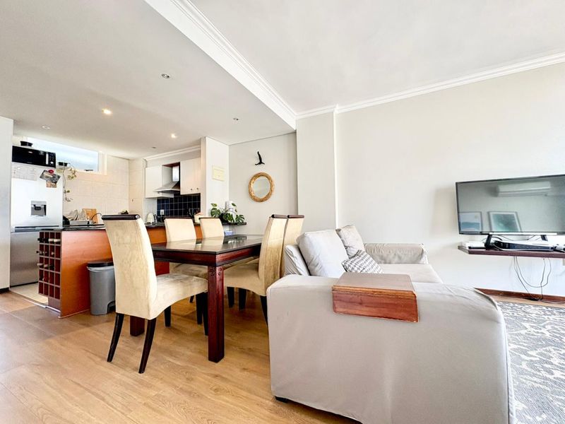 An open-plan living and dining area featuring laminate flooring, crown molding, and a functional kitchen with built-in cabinetry and a tiled backsplash.