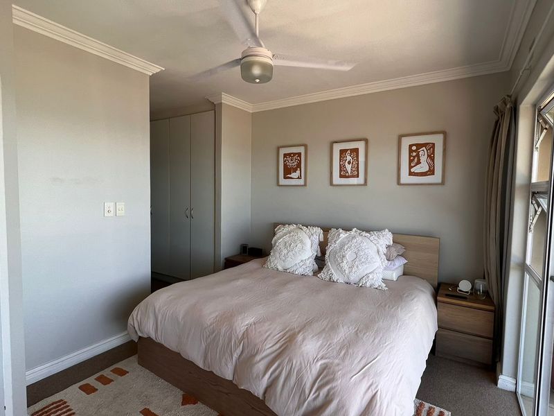 A well-maintained bedroom featuring built-in cupboards, a ceiling fan, and direct access to an outdoor balcony through a sliding glass door.