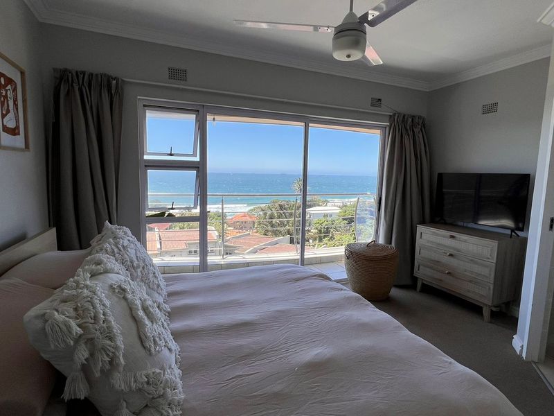 A well-maintained bedroom featuring carpeted floors, a ceiling fan, and large sliding glass doors that open to a balcony with ocean views.