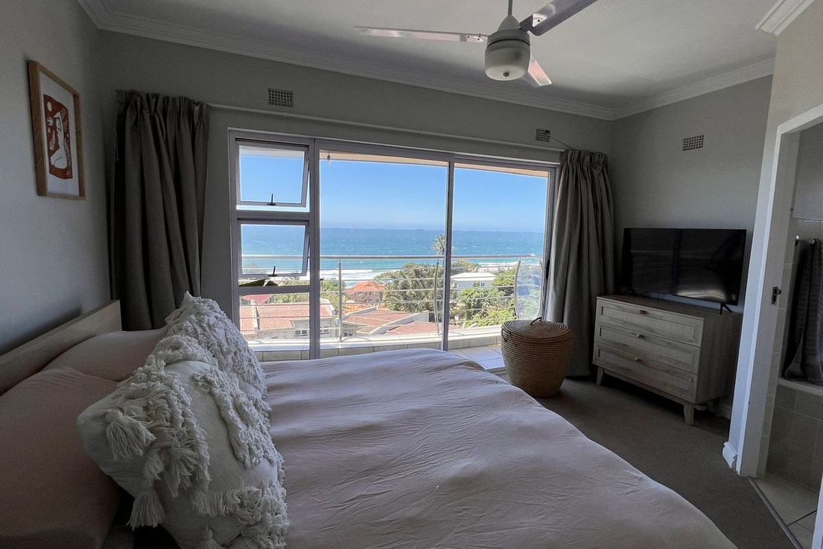 A well-maintained bedroom featuring carpeted floors, a ceiling fan, and large sliding glass doors that open to a balcony with ocean views.