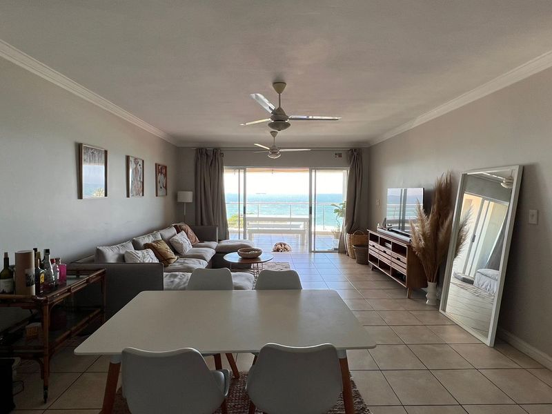 Spacious open-plan living and dining area featuring tiled floors, ceiling fans, and large sliding doors leading to a balcony with ocean views.