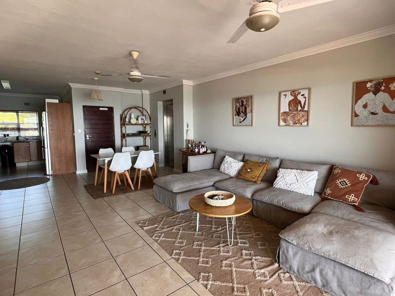 Spacious open-plan living and dining area featuring neutral tiled flooring, ceiling fans, and direct access to the kitchen and elevator.