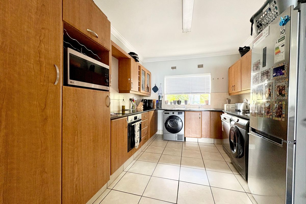 A functional kitchen featuring wood-finish cabinetry, laminate countertops, built-in oven and microwave, and tiled flooring with integrated laundry appliance space.