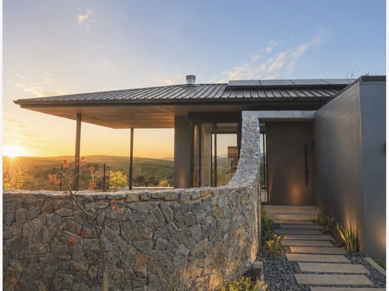 Modern architectural entrance featuring a striking curved stone wall, paved walkway, and expansive views at sunset.