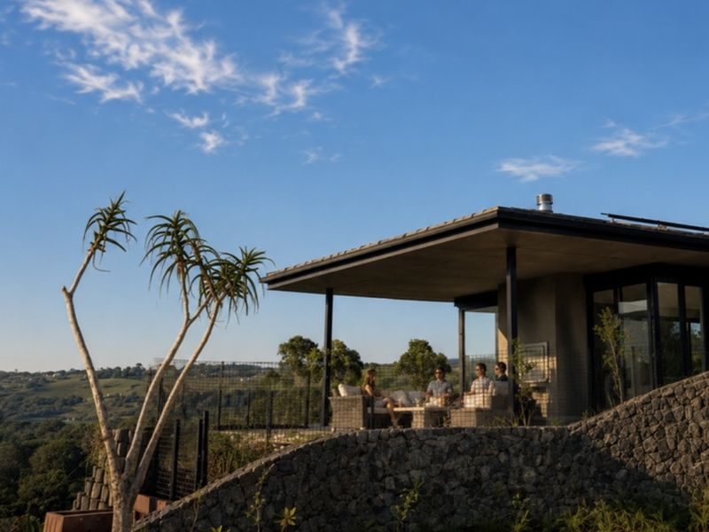 A modern covered patio featuring a stone retaining wall, concrete roof structure, and expansive views of the surrounding landscape.