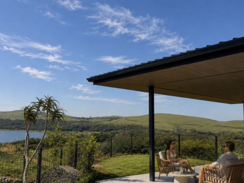 A modern covered patio area overlooking a swimming pool with expansive views of the surrounding landscape and lake.