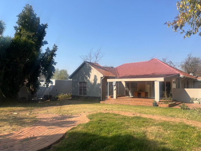 Rear view of the house featuring a covered patio, brick paved walkway, and a spacious garden area with established trees.