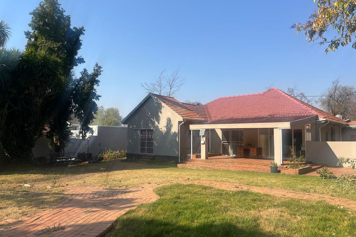Rear view of the house featuring a covered patio, brick paved walkway, and a spacious garden area with established trees.