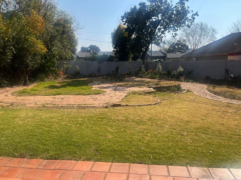 A spacious rear garden featuring a brick-paved pathway, established lawn, and perimeter walling, offering potential for landscaping and outdoor improvement.