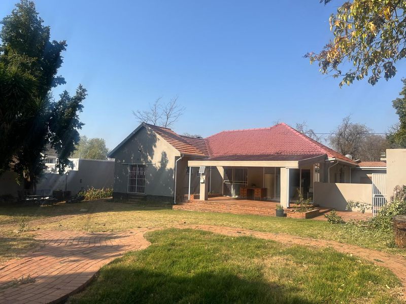Rear view of the house featuring a covered brick-paved patio, tiled roof, and a spacious garden with a paved walkway.