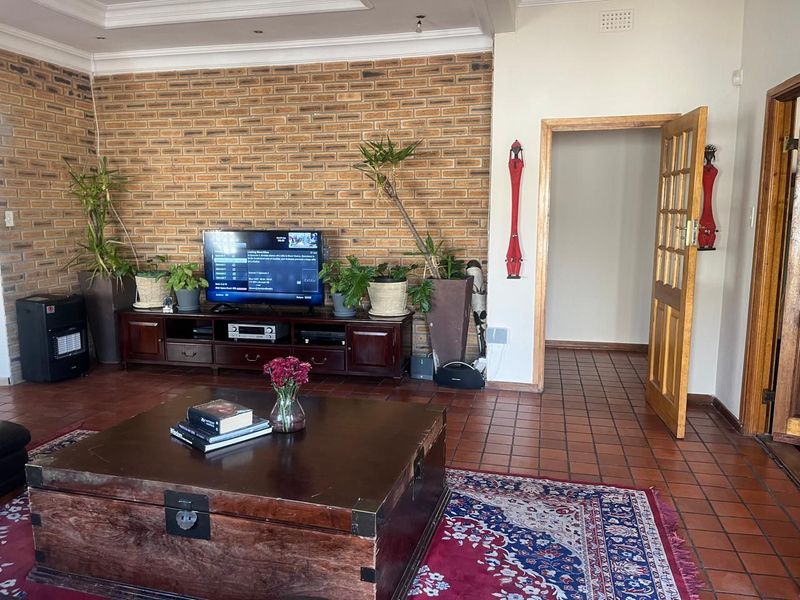 Living room featuring a prominent exposed brick wall, terracotta tile flooring, and a recessed ceiling design with a classic timber door.