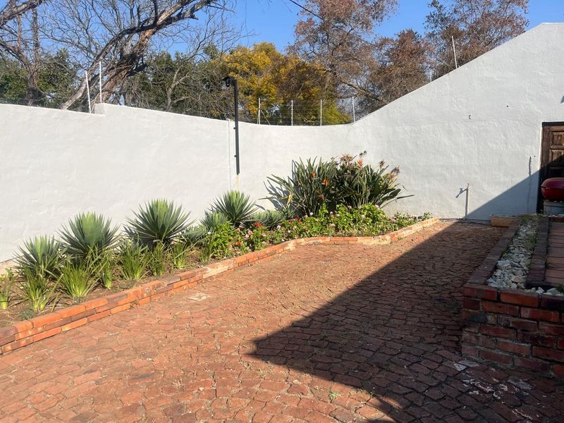 A private garden area featuring brick paving, established garden beds with mature plants, and a secure perimeter wall with electric fencing.