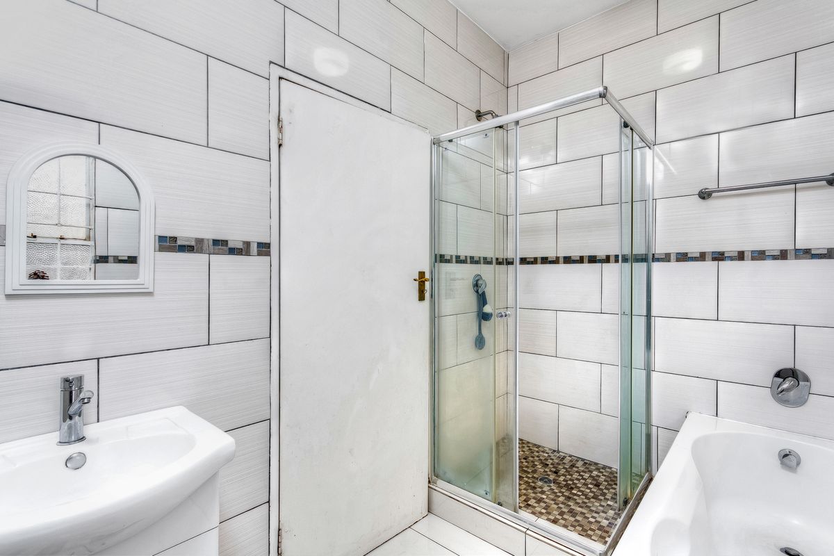 A functional bathroom featuring a shower enclosure, bathtub, and vanity basin with neutral wall tiling and mosaic accents.