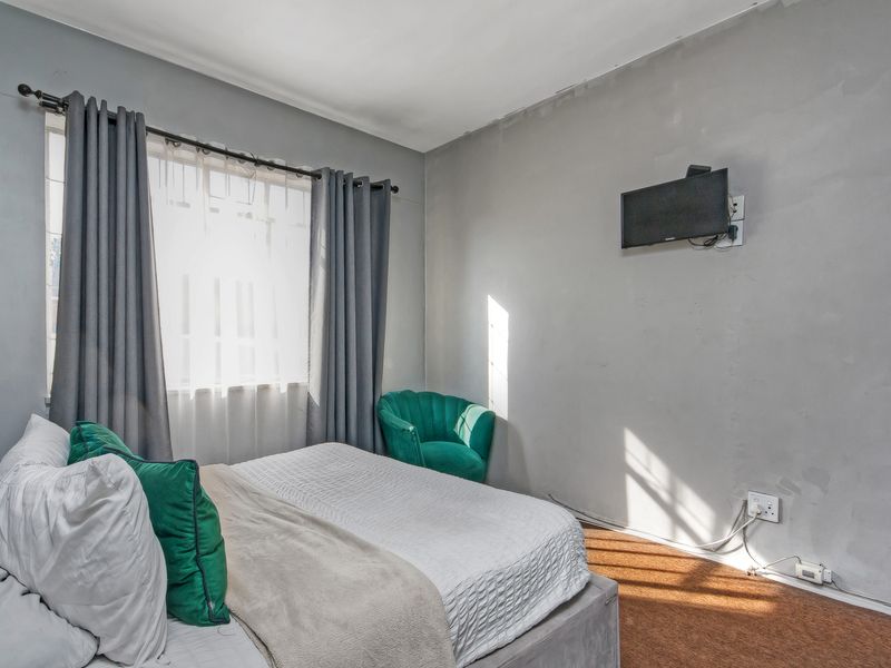A bedroom featuring grey walls, a window with curtains, and wall-mounted television connectivity. The room requires cosmetic updates to the walls and flooring.