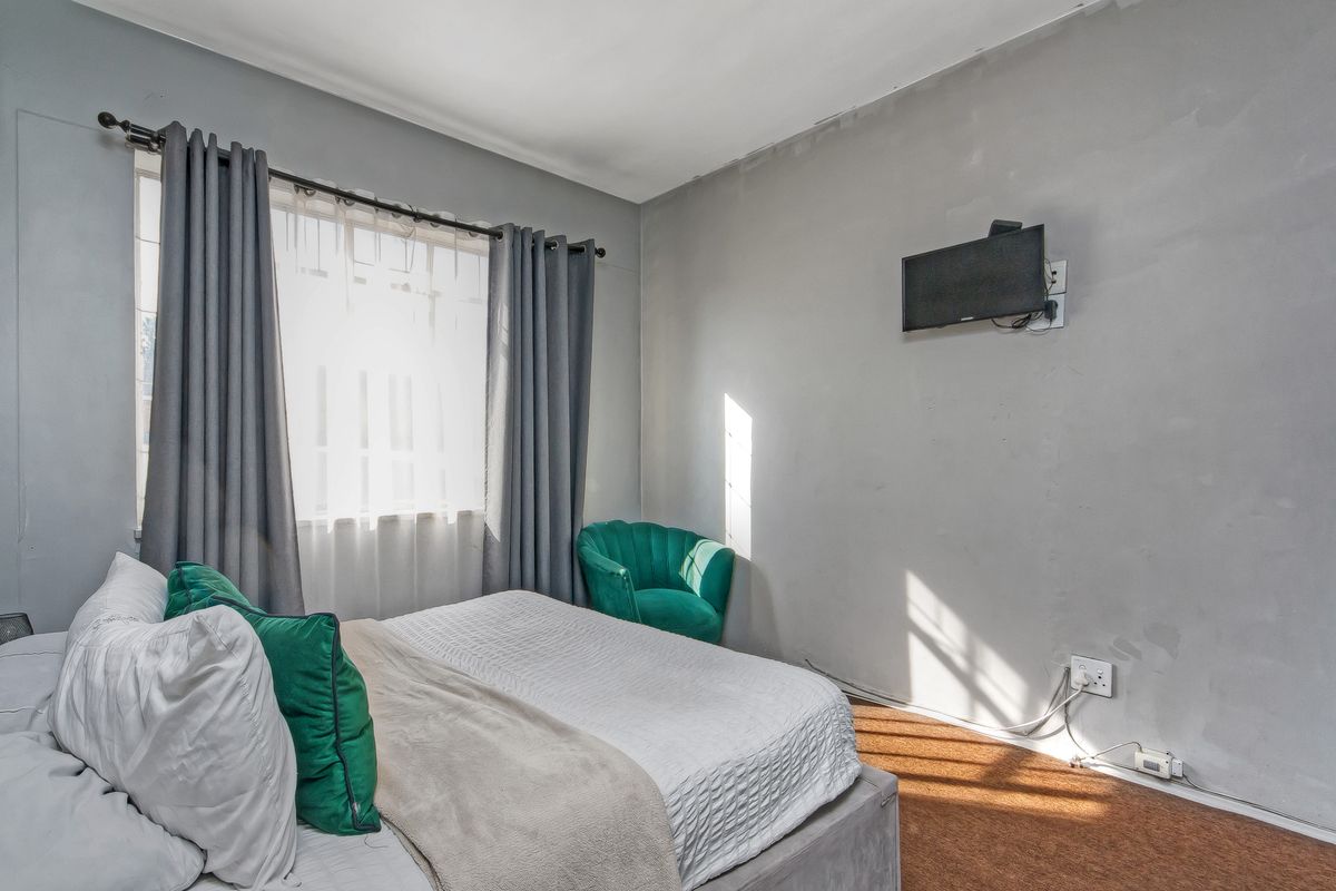 A bedroom featuring grey walls, a window with curtains, and wall-mounted television connectivity. The room requires cosmetic updates to the walls and flooring.
