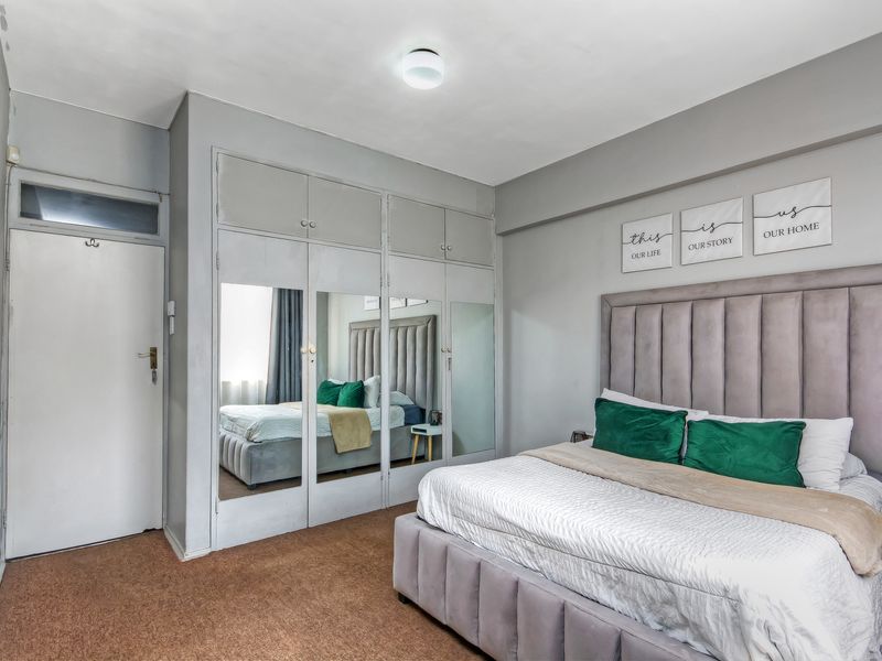 A bedroom featuring built-in cupboards with mirrored doors, a transom window above the door, and carpeted flooring.