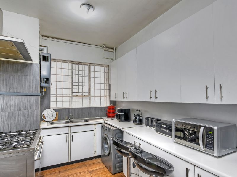 Functional kitchen featuring white cabinetry, gas stove with extractor, stainless steel sink, and tiled splashback, with integrated space for laundry appliances.
