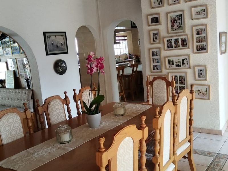 Dining room featuring exposed timber ceiling beams, ceramic tiled flooring, and arched architectural openings leading to the kitchen area.
