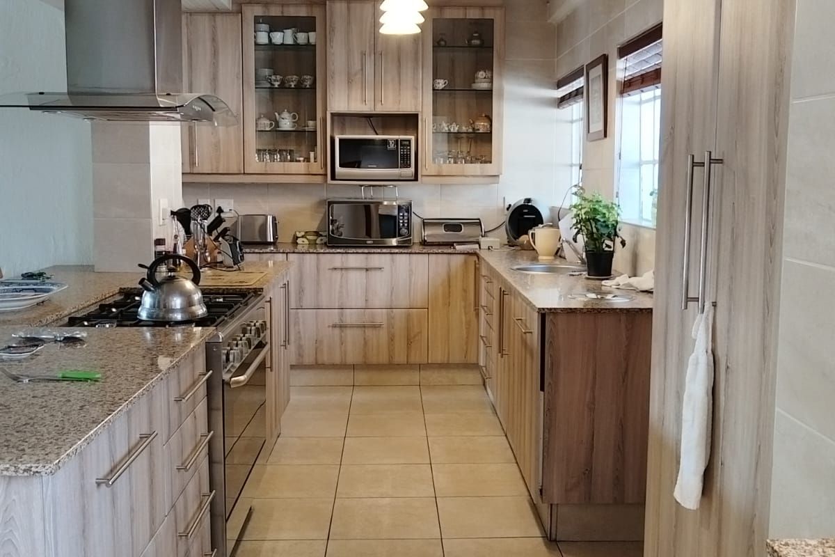 A well-appointed kitchen featuring timber-look cabinetry, granite countertops, a gas hob with stainless steel extractor, and integrated appliances.