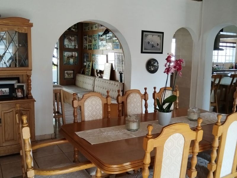 Dining room featuring exposed timber ceiling beams, ceramic floor tiles, and arched doorways leading to adjacent living and kitchen areas.