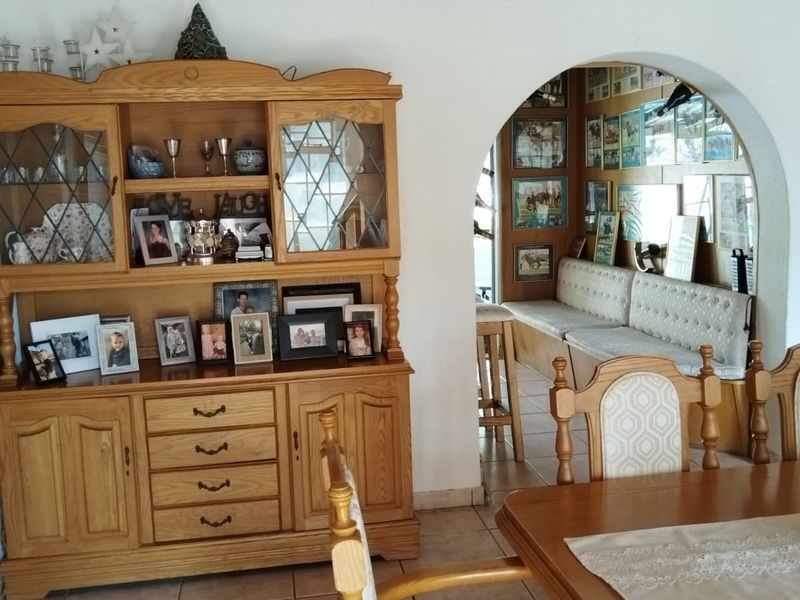 Dining area featuring exposed timber ceiling beams, tiled flooring with decorative inlays, and an arched doorway leading to a secondary seating space.
