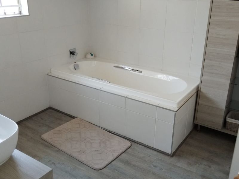 A well-maintained bathroom featuring a built-in bathtub, tiled walls, and rustic exposed timber ceiling beams, creating a clean and functional space.
