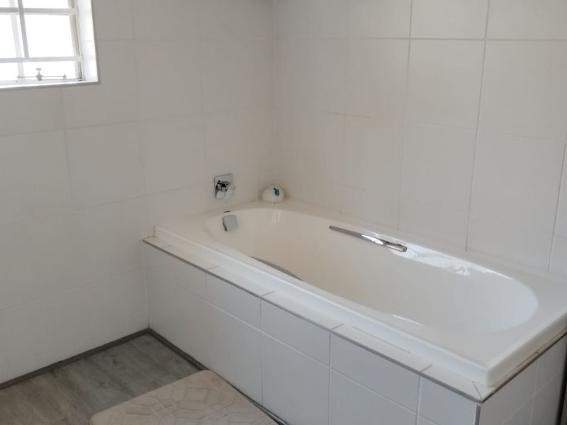 A clean bathroom featuring a built-in bathtub, white tiled walls, and rustic exposed timber ceiling beams, providing a bright and functional space.
