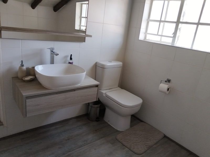 A modern bathroom featuring a vessel sink on a floating vanity, tiled walls, and wood-look laminate flooring.
