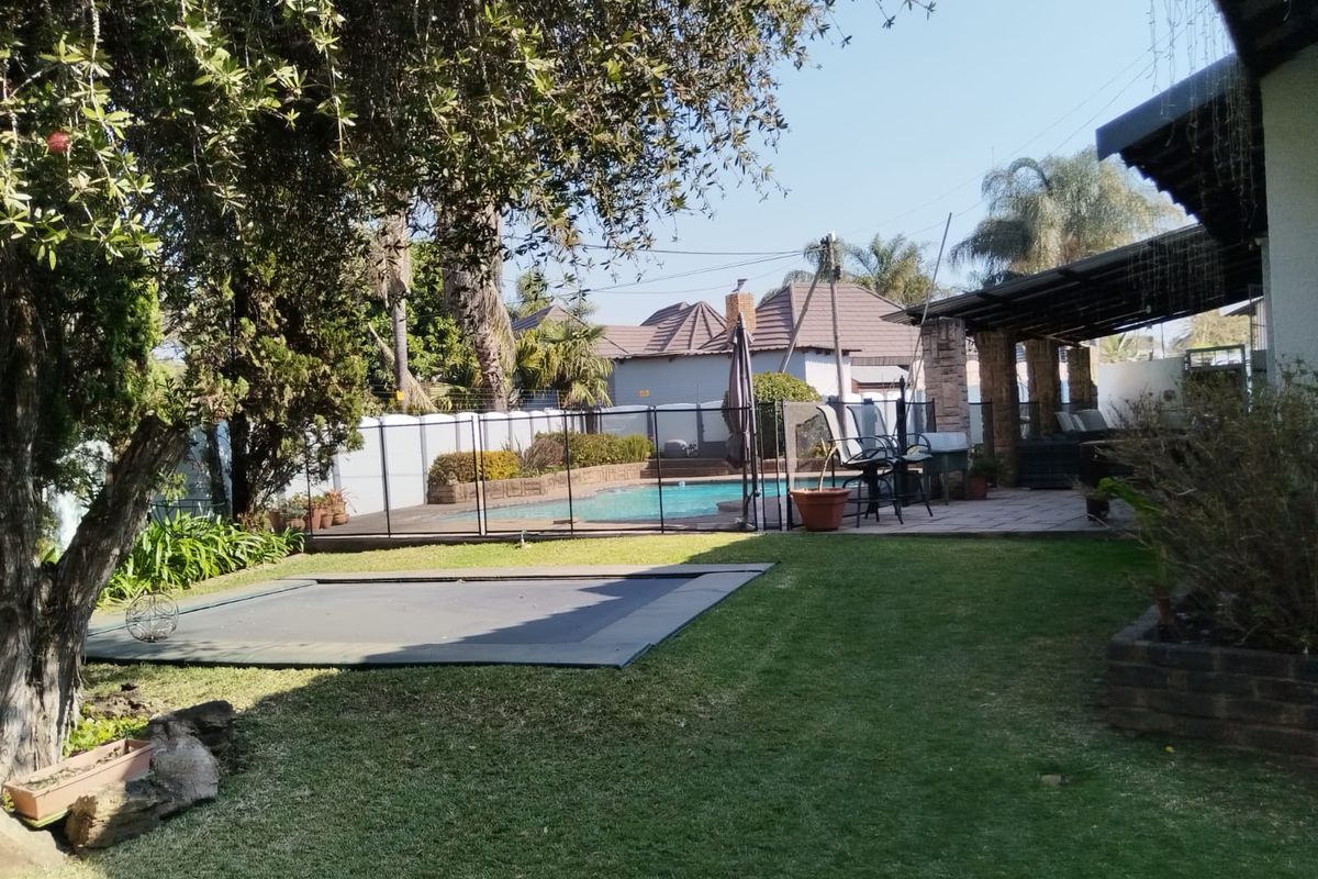 A spacious rear garden featuring a swimming pool with safety fencing, a covered patio area, and a well-maintained lawn.