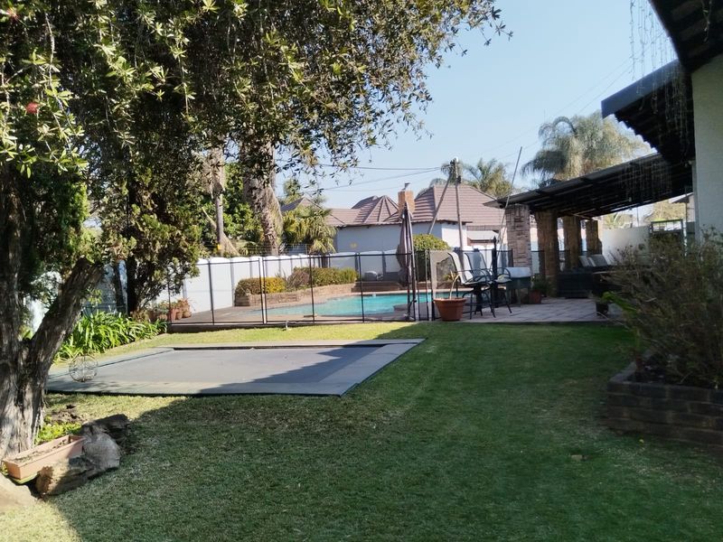 A spacious rear garden featuring a swimming pool with safety fencing, a covered patio area, and a well-maintained lawn.