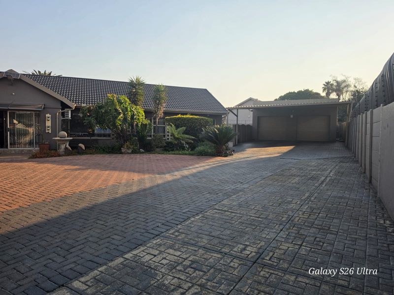Front exterior view of the property featuring a spacious paved driveway, double garage, and established garden area.