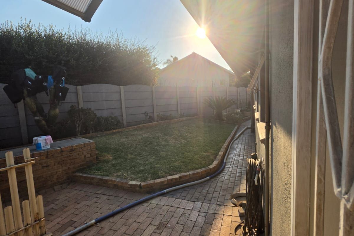 A rear garden area featuring brick paving, a precast concrete boundary wall, and a covered patio section with a polycarbonate roof.
