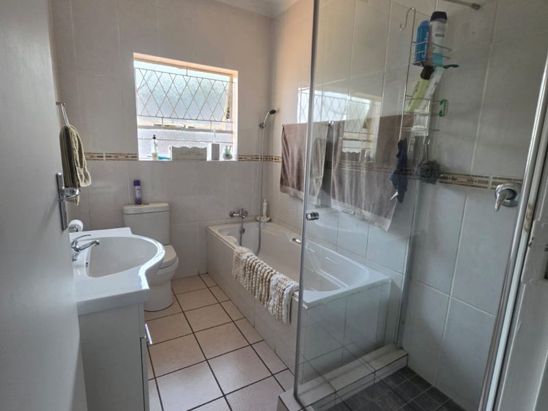 A functional bathroom featuring a separate bathtub and glass-enclosed shower, tiled walls and floors, and a pedestal basin.