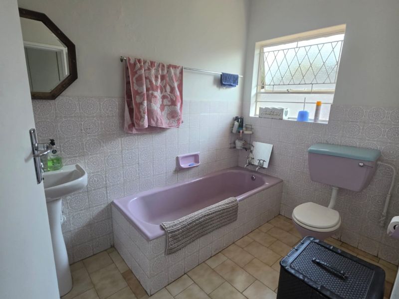 A dated bathroom featuring a pastel-colored bathtub and toilet suite, pedestal basin, and tiled finishes, offering potential for a modern renovation.