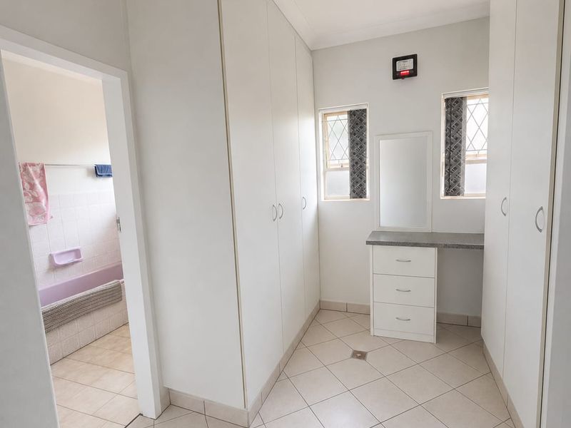 A dressing area featuring extensive built-in cupboards, tiled flooring, and a vanity unit, with direct access to an adjoining bathroom.