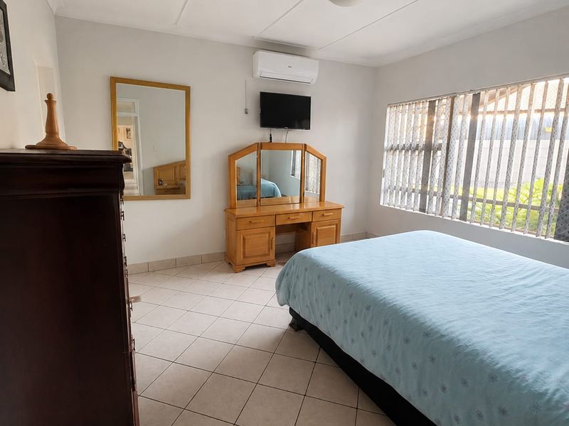 A bedroom featuring tiled flooring, a split-system air conditioner, and vertical blinds, offering a functional and well-lit living space.