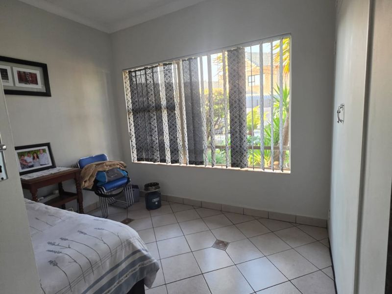 A bedroom featuring tiled flooring, built-in cupboards, and vertical blinds, offering a functional space with natural light.