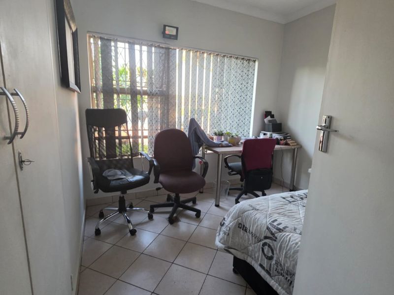 A compact bedroom featuring tiled flooring, a built-in cupboard, and a window with vertical blinds and security bars.