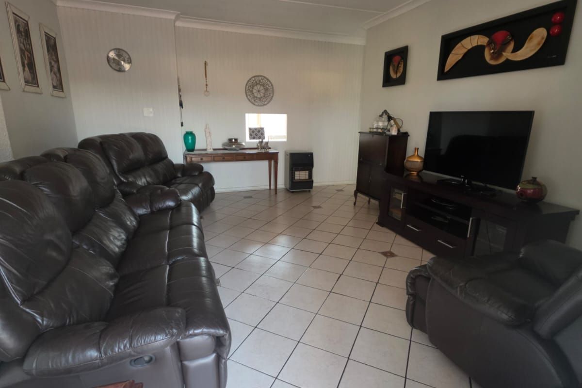A spacious living room featuring neutral tiled flooring and a panelled ceiling, providing a functional and well-maintained living area.