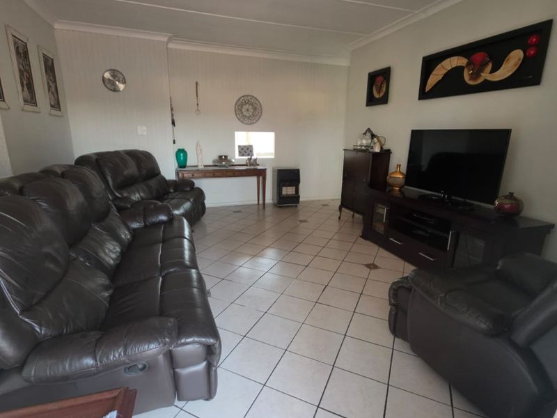 A spacious living room featuring neutral tiled flooring and a panelled ceiling, providing a functional and well-maintained living area.