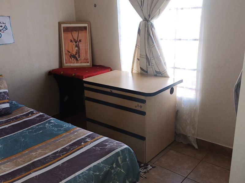 A compact bedroom featuring tiled flooring and a window with security bars, providing a functional living space.