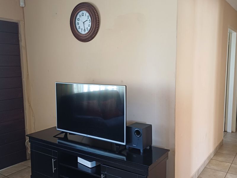 A living area featuring tiled flooring and access to an adjacent bedroom, showing signs of wear on the wall surfaces.