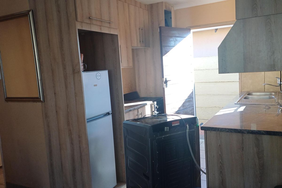 A functional kitchen featuring wood-look laminate cabinetry, integrated sink, and extractor fan, with direct access to an outdoor area.