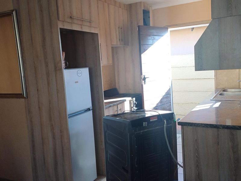 A functional kitchen featuring wood-look laminate cabinetry, integrated sink, and extractor fan, with direct access to an outdoor area.