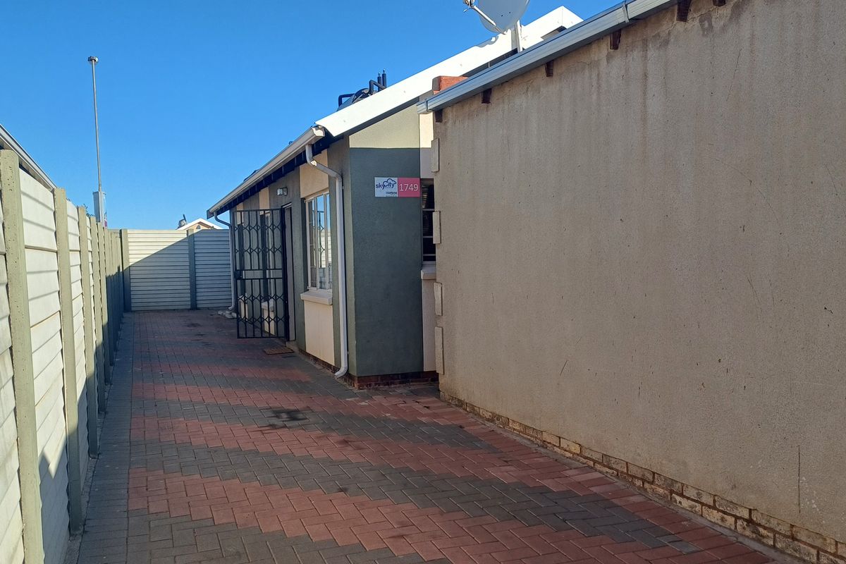 A side view of the property featuring paved pathways, a precast concrete boundary wall, and a secure entrance gate.