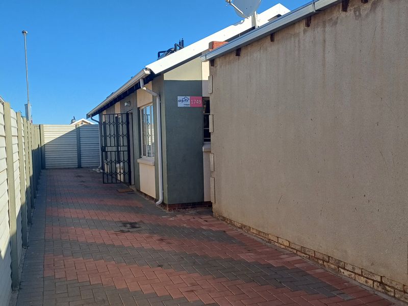 A side view of the property featuring paved pathways, a precast concrete boundary wall, and a secure entrance gate.