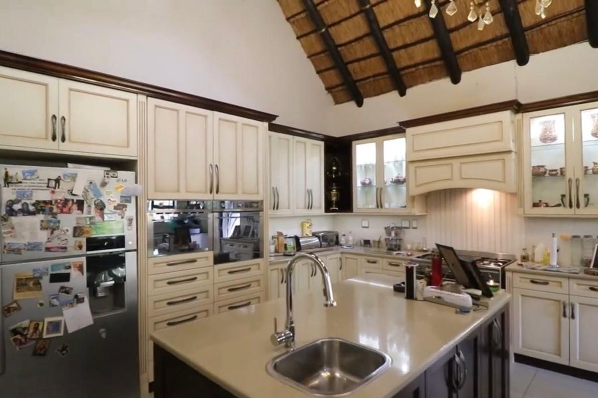 Spacious kitchen featuring custom cabinetry, stone countertops, a central island with sink, and a distinctive high-vaulted thatch roof with exposed timber beams.